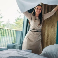 Fröhliche Zimmermädchen zieht energisch ein Bettlaken glatt, symbolisch für den zuverlässigen und freundlichen Service von S.K. Reinigungsservice Leipzig e.K.